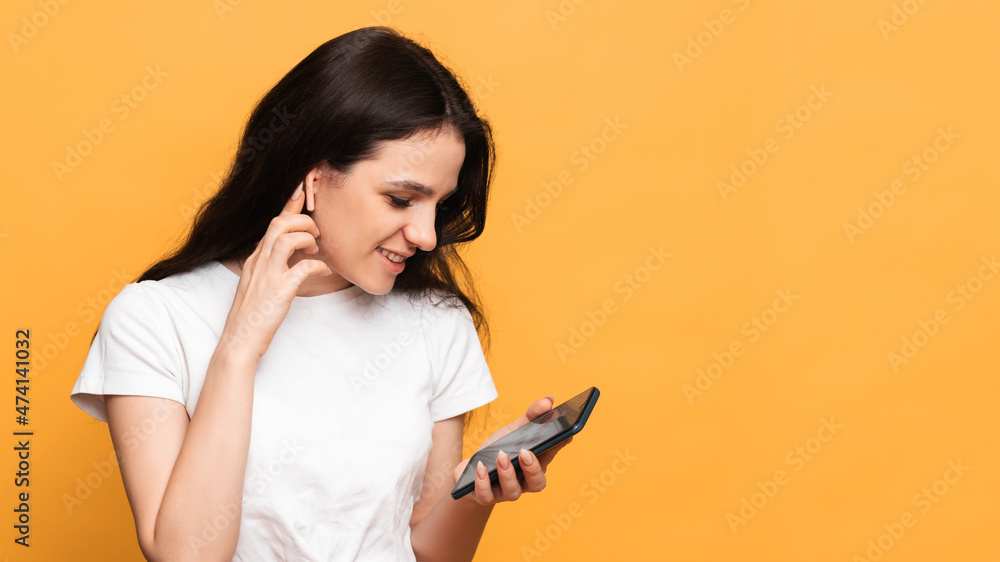 A smiling woman is holding a smartphone on which she records an audio message or talks in an audio chat, standing on a yellow background. A copy of the space. Space for text A smiling woman is holding a smartphone on which she records an audio message or talks in an audio chat, standing on a yellow background. A copy of the space. Space for text