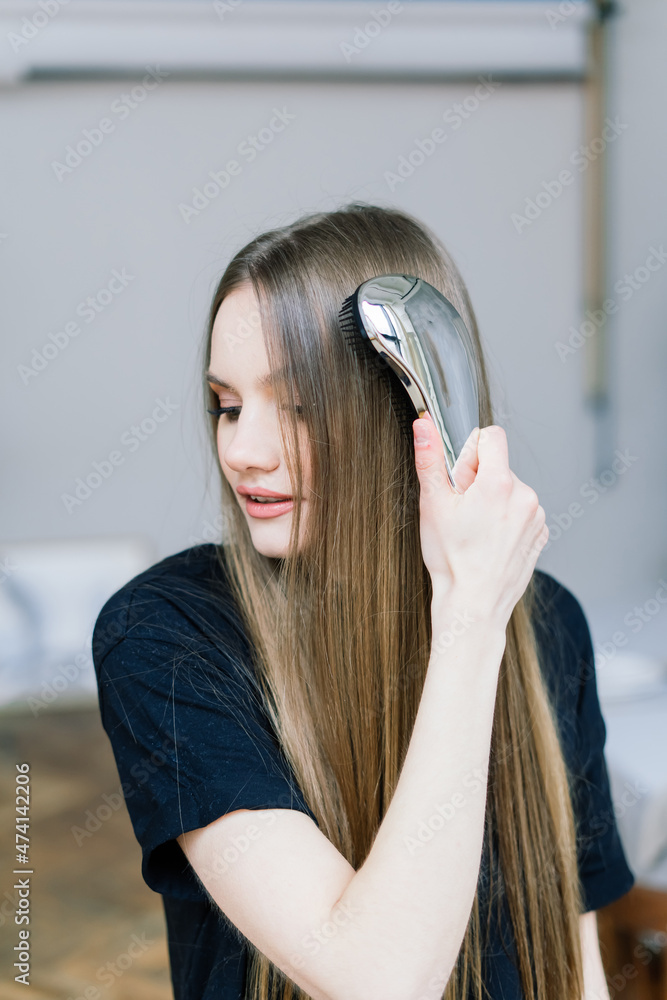 Fototapeta premium Girl touching her hair and smiling while posing at interior looking in the mirror