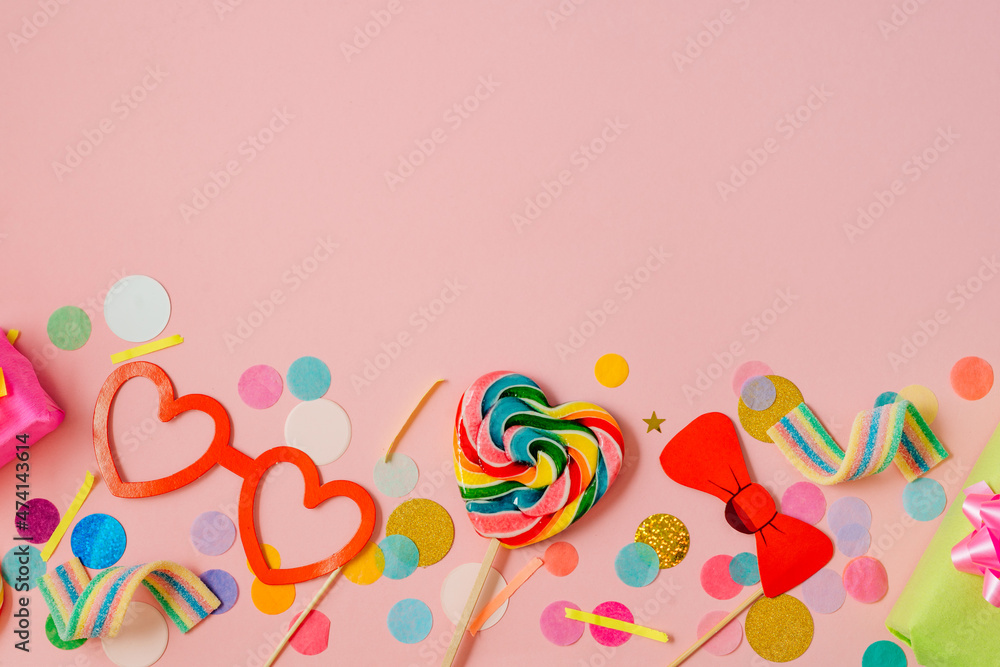 Heart shaped lollypop and decorative paper eye glasses, gift boxes on pink background with confetti