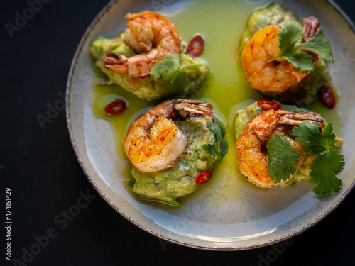 Appetizer with shrimps served with guacamole and greens on white plate on black background. Delicious, beautiful, healthy snack. Modern cuisine