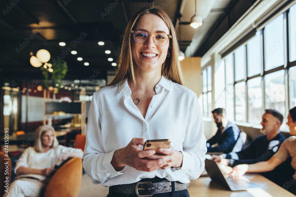 Leinwandbild Motiv - Jacob Lund : Young businesswoman holding a smartphone in a co-working space