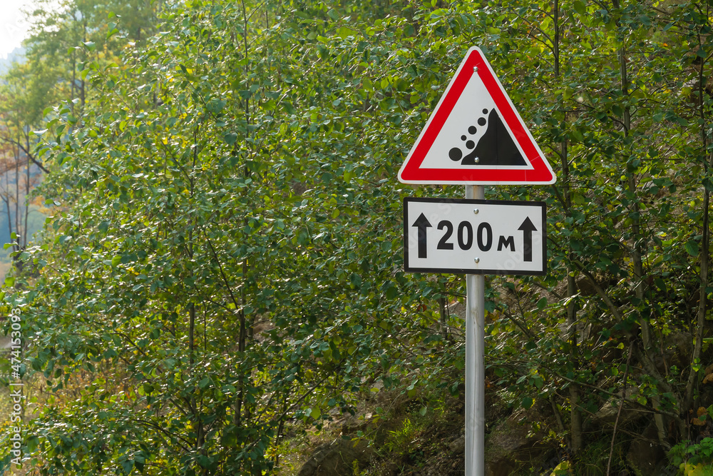 Close-up of a warning road sign rockfall on a background of trees with copy space