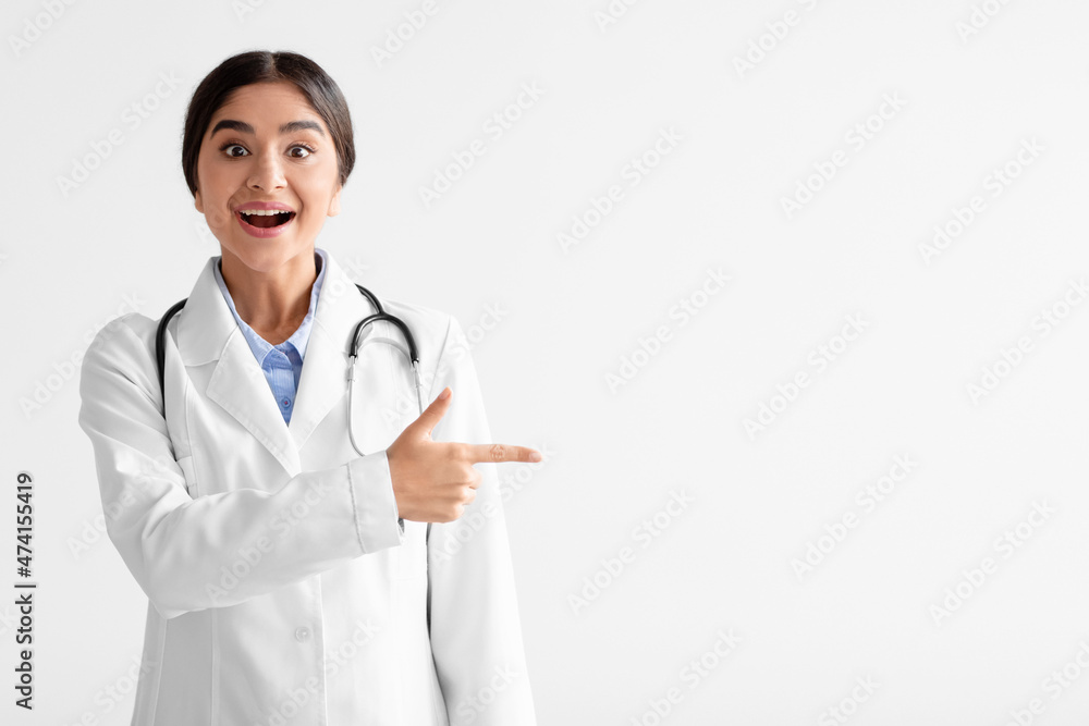 Surprised cheerful young indian woman in white coat with open mouth shows finger to empty space Surprised cheerful young indian woman in white coat with open mouth shows finger to empty space
