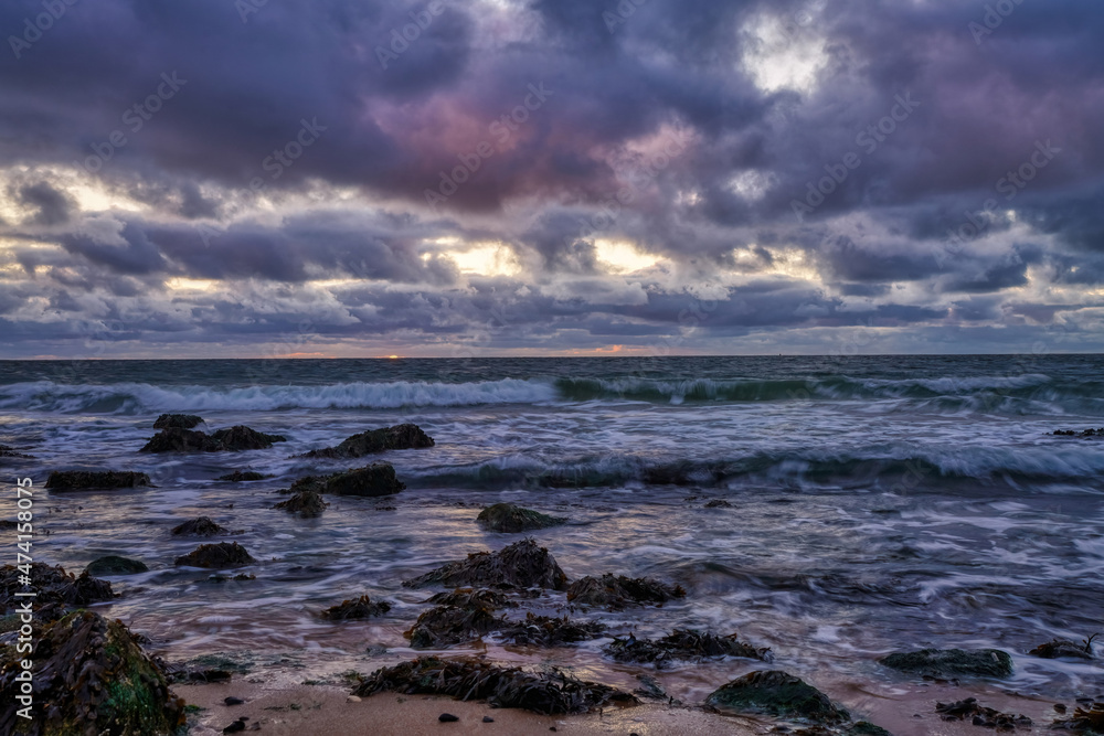 Landscape, seascape sunset on the coast of Huisduinen, the Netherlands. long exposer of waves, dramatic sky, detailed, seaweed, rocks