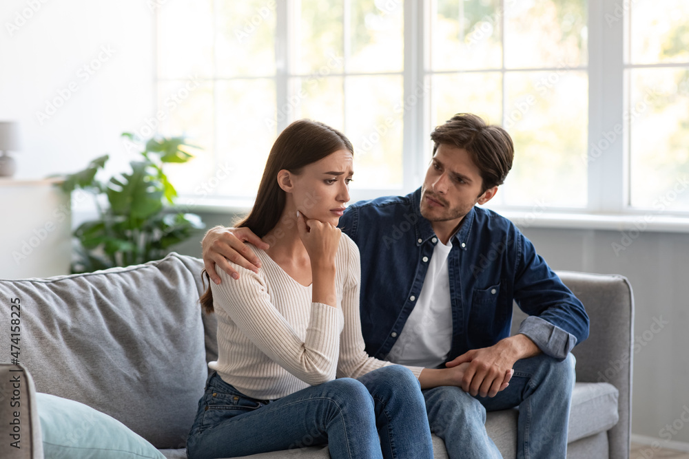 Serious careful young european guy calms upset unhappy lady in living room interior Serious careful young european guy calms upset unhappy lady in living room interior