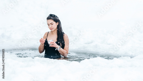 Girl with dessert in frozen lake ice hole. Woman hardening the body in cold water. Successful woman concept © Augustas Cetkauskas