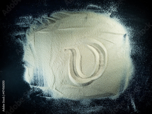 Greek letter upsilon written on the white sand with black background photo