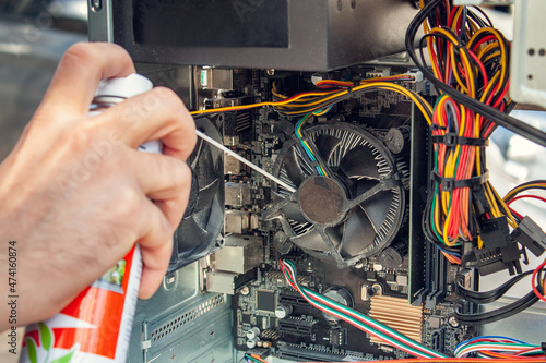 Maintenance and cleaning of the insides of the computer. Man's hand holds a cylinder of compressed air and cleans the insides of the computer photo