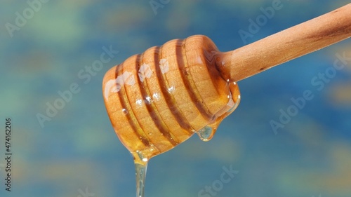 Close up fresh fluid honey pouring and flowing from wooden dipper spoon over blue background with copy space. honey dipping from a wooden honey spoon. Healthy food concept, diet