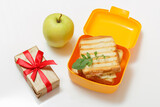 Yellow lunch box with toasted slices of bread, cheese and green apple.