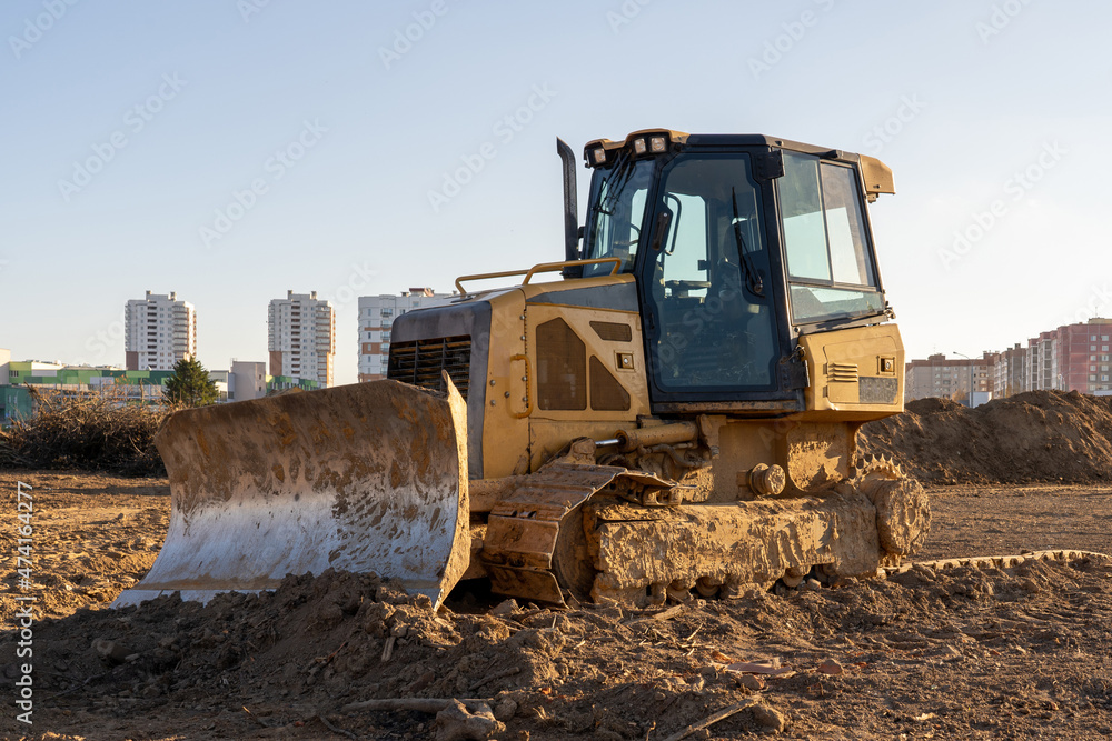 Photo of a yellow muddy excavator digging the ground at a construction site at the background of city. Constructional concept Photo of a yellow muddy excavator digging the ground at a construction site at the background of city. Constructional concept
