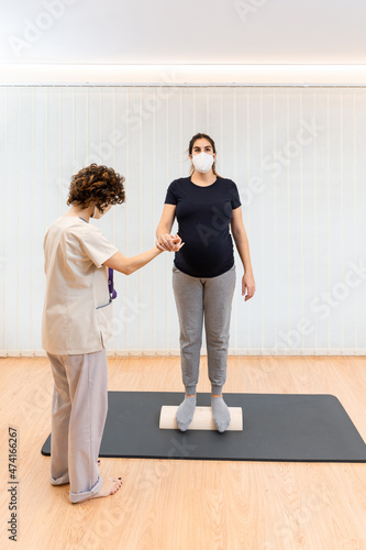 pregnant woman standing on a proprioceptive trunk for lumboabdominal and perineal walls with physiotherapist photo