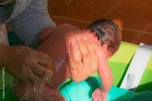 madre frota la espalda de su hijo recién nacido mientras le ducha photo