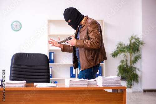 Young man in balaclava stealing information from the office