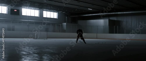 WIDE HANDHELD Determined professional ice hockey player practices at the indoor rink alone. Shot with 2x anamorphic lens photo