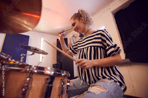 Low angle portrait of smiling young woman playing drums with contemporary music band during rehearsal or concert in studio, copy space