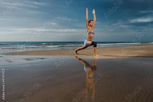 Beautiful sporty fit yogini woman practices yoga asana Virabhadrasana - warrior pose , on the beach..