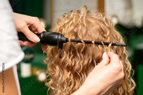 Photography Hands of hairstylist curl wavy hair of young woman using a curling iron for hair