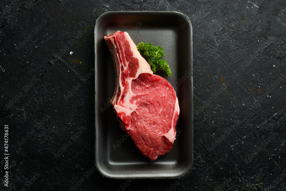 Beef fresh raw steak on the bone. On a black stone background. Organic food.
