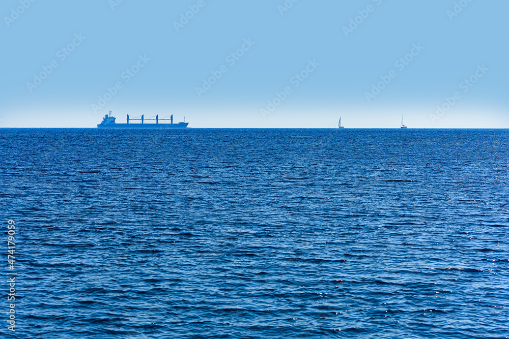 a cargo ship and two sailing yachts at the ocean a cargo ship and two sailing yachts at the ocean