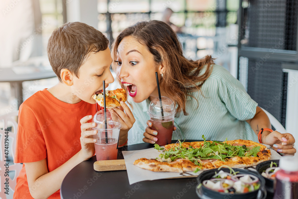 Mother and son eat delicious Italian pizza in a pizzeria or cafe. Joint leisure and fast food concept Mother and son eat delicious Italian pizza in a pizzeria or cafe. Joint leisure and fast food concept