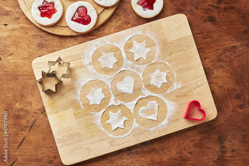 Wooden cutting board with powdered sugar and Linzer cookies, baking decoration process photo