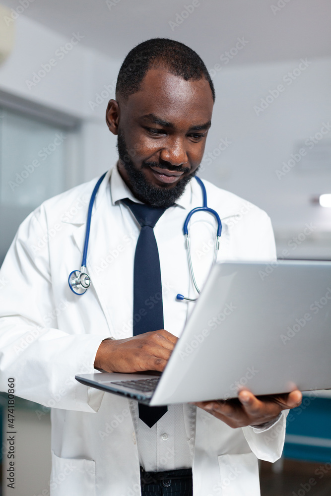 African american practitioner doctor typing medical expertise on laptop computer analyzing healthcare treatment report during clinical appointment. Therapist man working in hospital office African american practitioner doctor typing medical expertise on laptop computer analyzing healthcare treatment report during clinical appointment. Therapist man working in hospital office