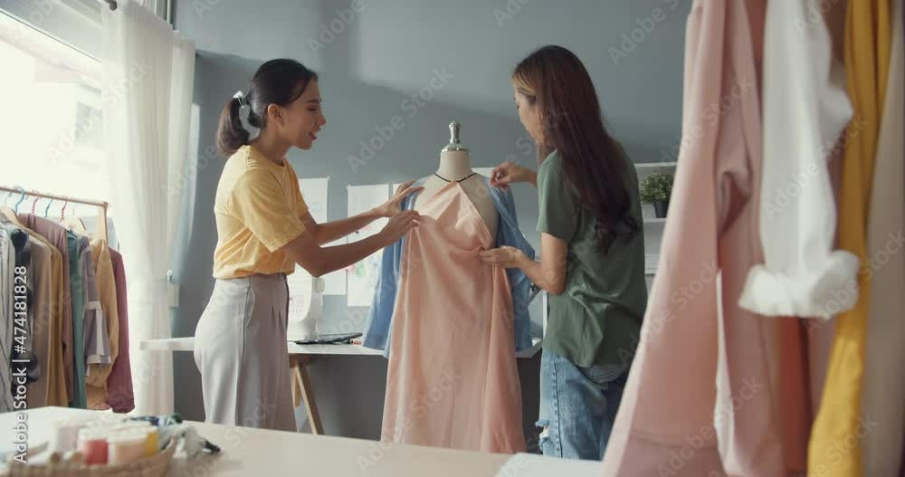 Two professional Asia cheerful lady fashion designer teamwork with casual pin on fabric share idea create beautiful dress on dummy in shop. Lady tailor business partner cloth shop start up business. Two professional Asia cheerful lady fashion designer teamwork with casual pin on fabric share idea create beautiful dress on dummy in shop. Lady tailor business partner cloth shop start up business.