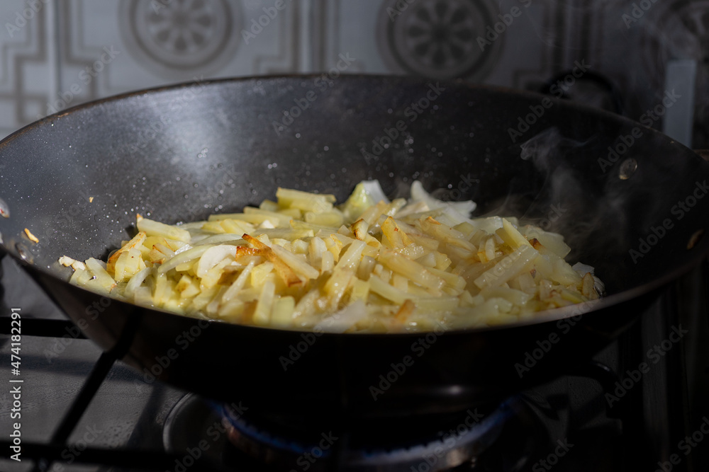 onion and friendose cut potato over vegetable oil in a black skillet onion and friendose cut potato over vegetable oil in a black skillet