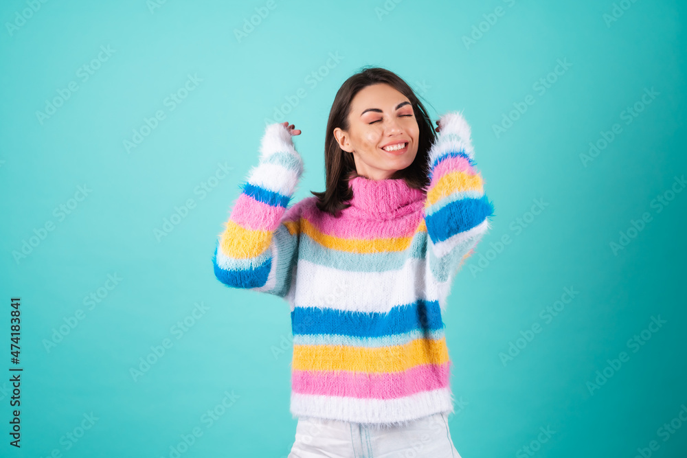 A young woman in a bright multi-colored sweater on a blue background laughs fervently, smiles, turns her head, her hair flies, her eyes are closed A young woman in a bright multi-colored sweater on a blue background laughs fervently, smiles, turns her head, her hair flies, her eyes are closed