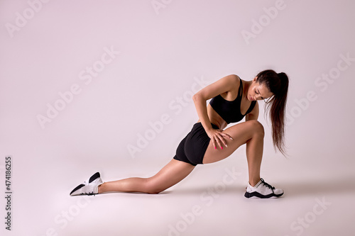 Side view Portrait of young brunette lady stretching legs before workout, isolated in studio on pink background. Fit athlete female in black top and shorts warming up legs muscles, doing lunges © alfa27