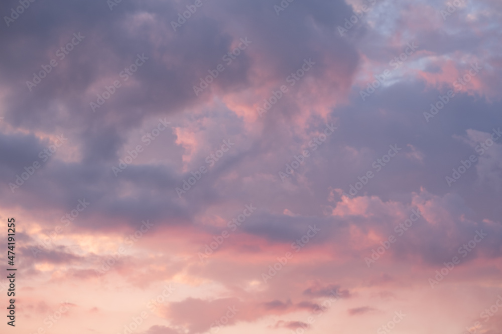 Moody sunset or sunrise sky with rays of light illuminating dark blue and bright and soft pink and orange clouds. no people, clouds only. High contrasts in a stormy sky