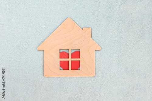 Wooden house symbol on light blue fabric textured background. A red heart is visible in the window of the house. Selective focus. The concept of peace and love in the family. Family dwelling
 photo