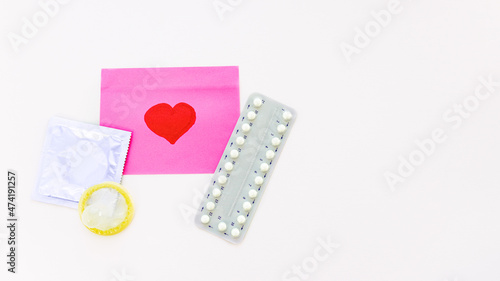 Packing of contraceptive pills and condoms on a white background next to lies a pink sticker with a red heart symbol. The concept of sexual education for adolescents. Contraceptive selection by partne photo