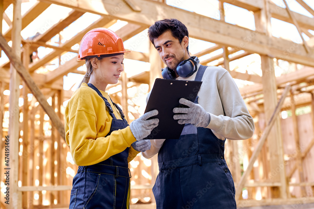 two smart architects constructors holding clipboard blueprints at construction site while discussing their work plan, have conversation, wearing working uniform and hardhat. architecture, building
