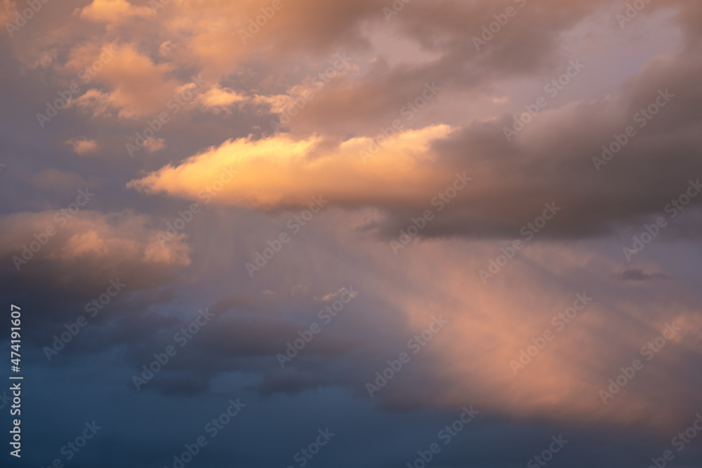 Moody sky with ray of light illuminating dark blue and bright orange clouds. clouds in a stormy sky. no people, clouds only. High contrasts in the sky