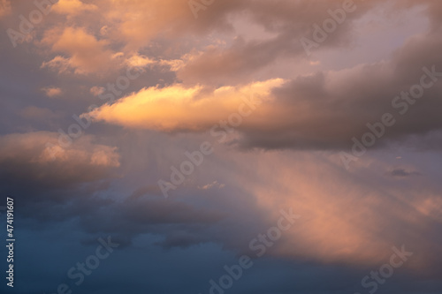 Moody sky with ray of light illuminating dark blue and bright orange clouds. clouds in a stormy sky. no people, clouds only. High contrasts in the sky