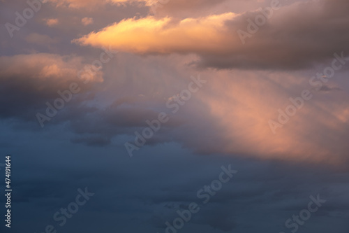 Moody sky with ray of light illuminating dark blue and bright orange clouds. clouds in a stormy sky. no people, clouds only. High contrasts in the sky