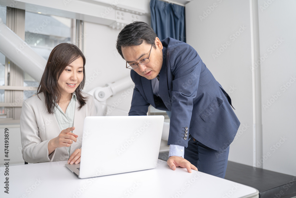 オフィスでノートパソコンを見ながら打ち合わせをする男女のビジネスマン オフィスでノートパソコンを見ながら打ち合わせをする男女のビジネスマン