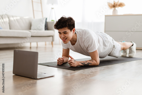 Sporty asian man doing plank watching tutorial on laptop