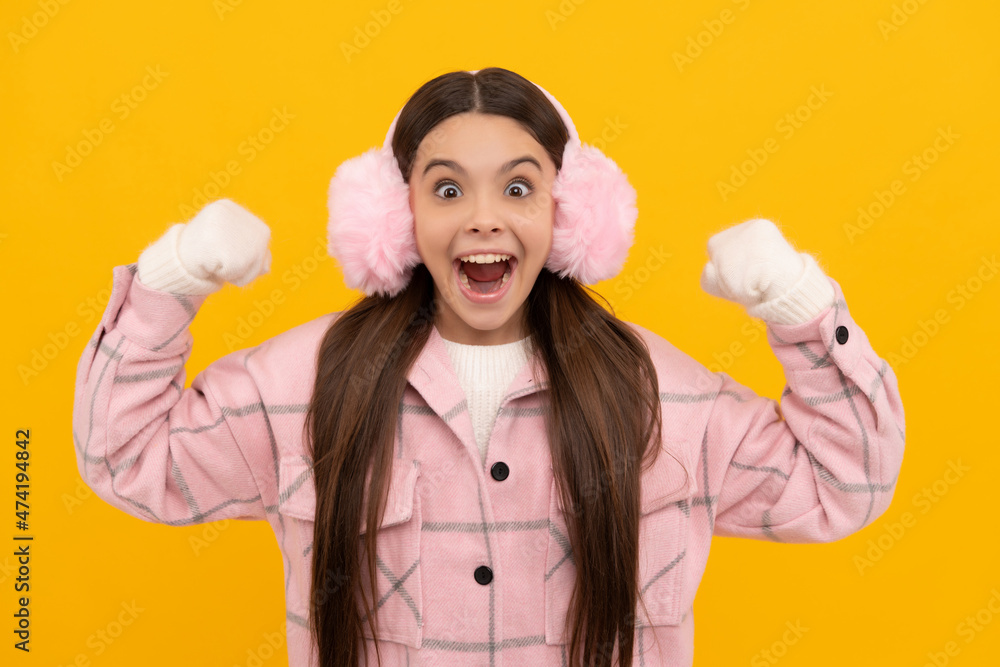 amazed kid in winter mittens and earmuffs on yellow background, winter fashion amazed kid in winter mittens and earmuffs on yellow background, winter fashion