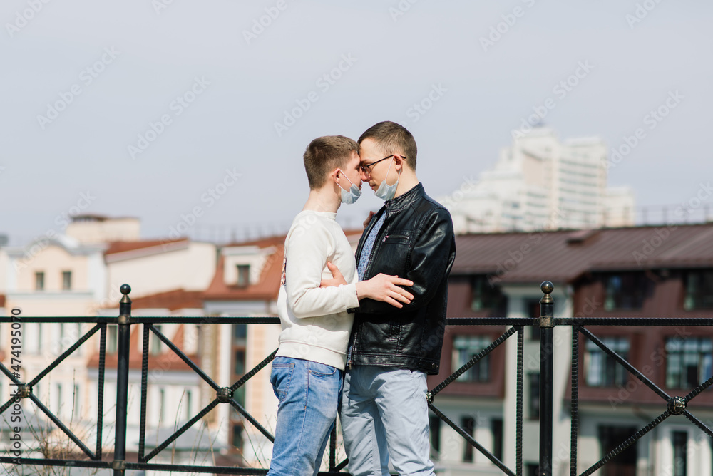 Young gay couple wearing medical mask hugging at city.