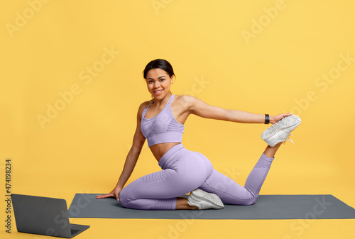 Training on isolation. Happy african american lady exercising and watching online tutorials on laptop, yellow background