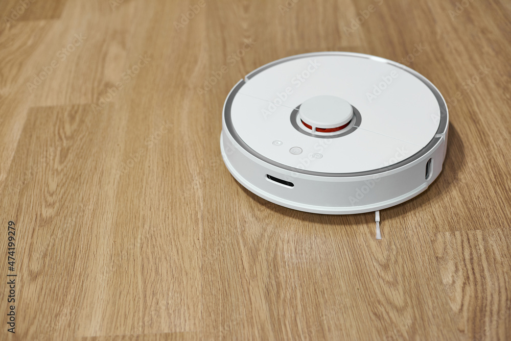 White robot vacuum cleaner on laminate flooring. White robot vacuum cleaner on laminate flooring.