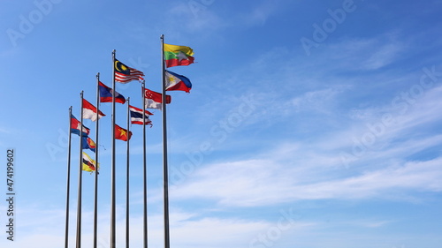  ASEAN flags flying on poles. Several multicolored ASEAN flags on metal poles flutter in the wind against the backdrop of a blue sky with thin white clouds with copy space. Selective focus photo