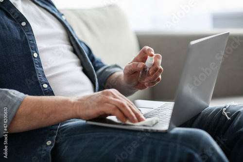 Male hands using disinfectant spray for cleaning laptop, cropped
