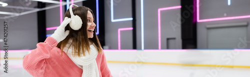 pleased woman in pink sweater adjusting white ear muffs, banner.