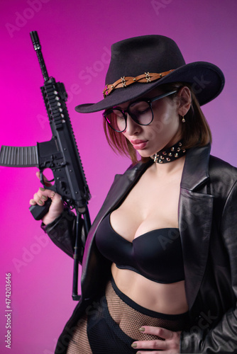 sexy woman with an automatic rifle in black leather clothes and hat