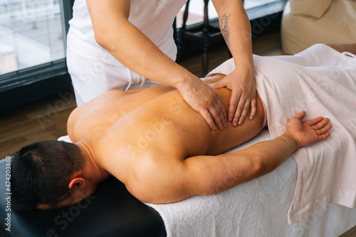 High-angle view of professional male masseur with strong hands massaging side of back to muscular sports man lying on stomach, at massage table in luxury salon. Concept of healthy lifestyle and rest.