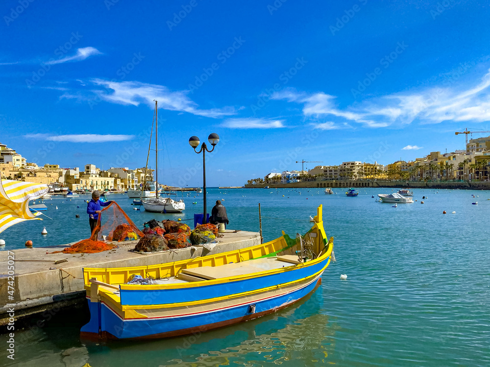 Bright colored boat and fishermen with nets in the port on the island of Malta